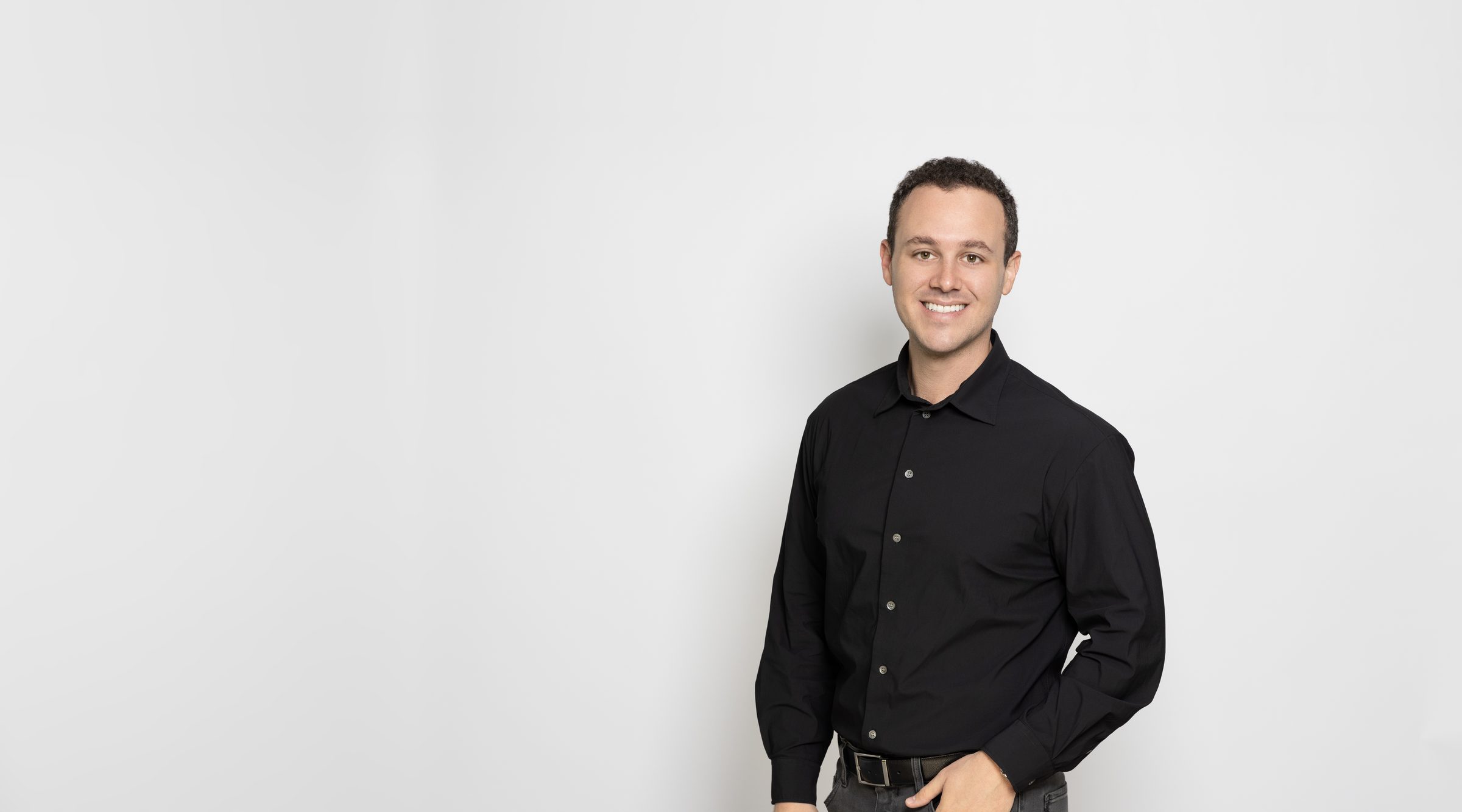 Dr. Doug Shapiro, smiling, in a black button-down shirt against a light gray backdrop